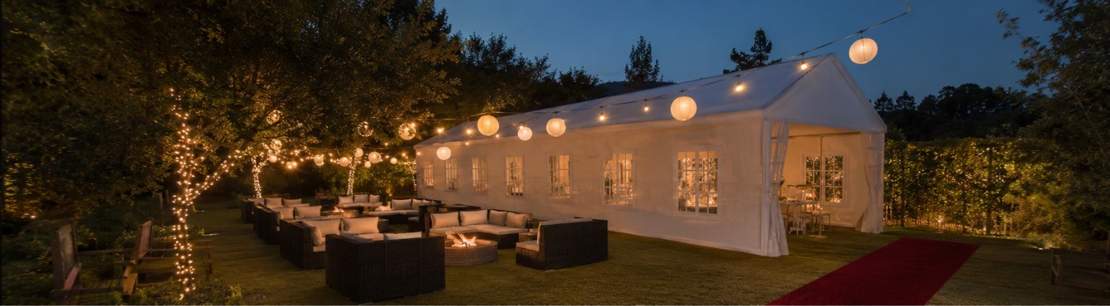 A tenda iluminada ao anoitecer, rodeada por lanternas e árvores maduras